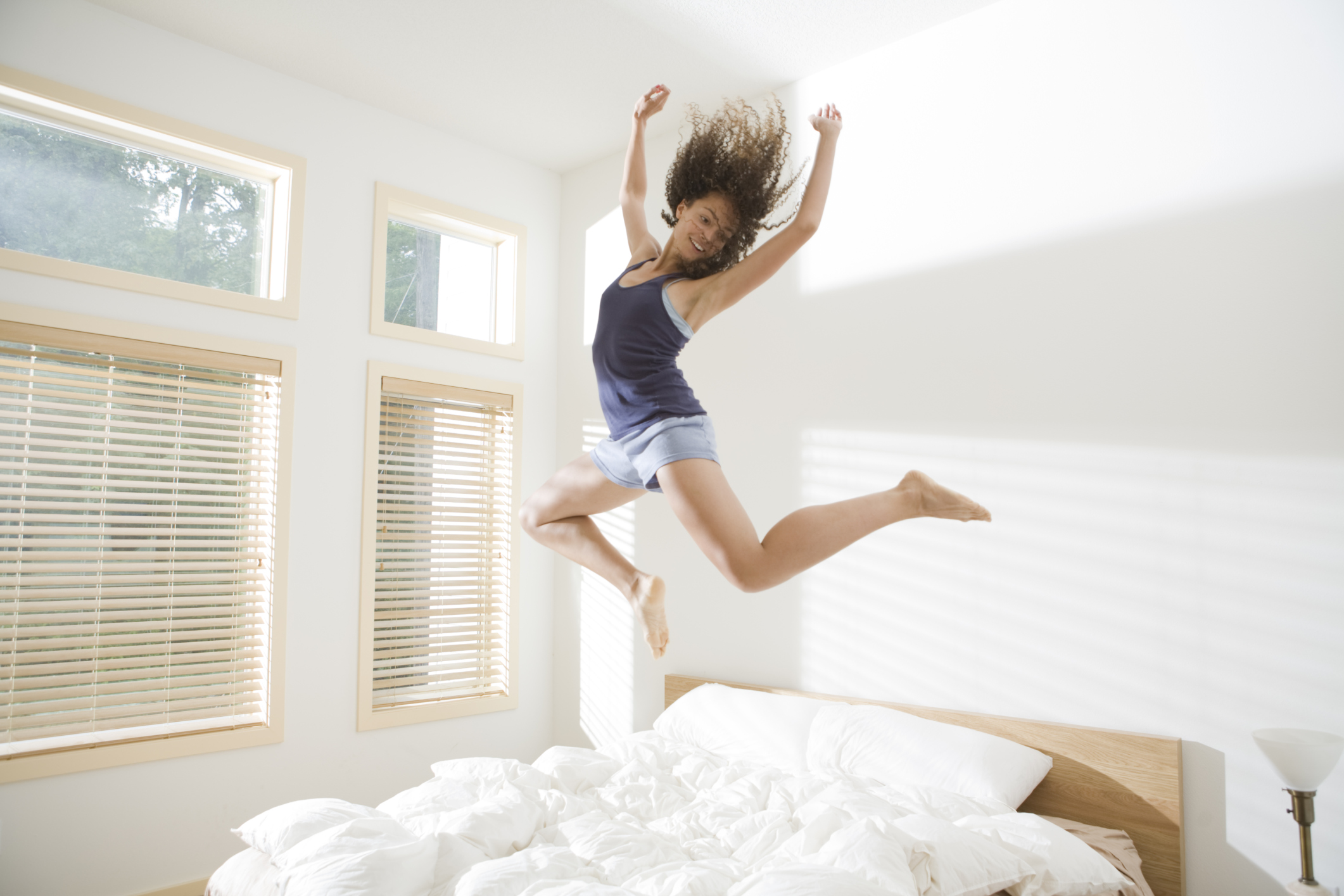 Жизнь в доме наполненным. Девушка в прыжке. Девушка прыгает. Девушка прыгает на кровати. Бодрость утром.